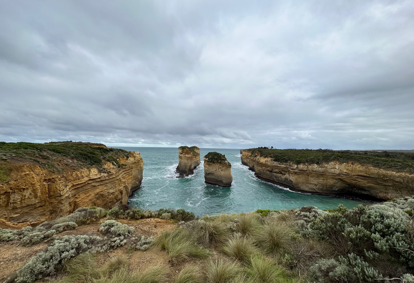 Two tall rock formations in the ocean between two cliffs.